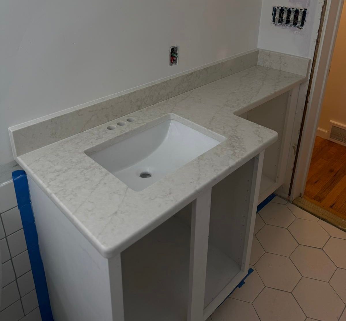 White bathroom vanity with a built-in sink, countertop, and open cabinet shelves, viewed from an angle.