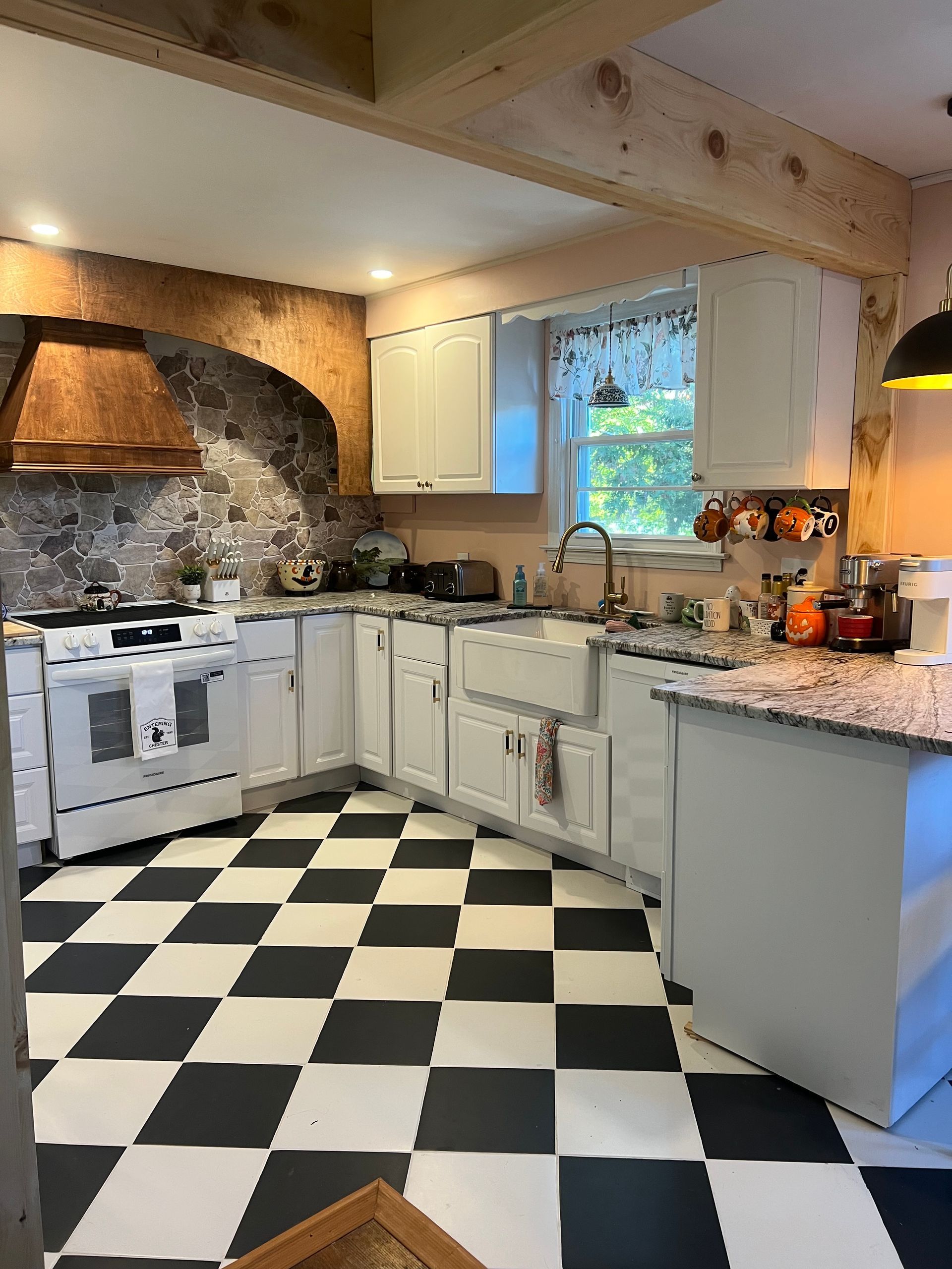 Cozy rustic kitchen with black-and-white checkered floor, white cabinets, stone backsplash, and wood beams