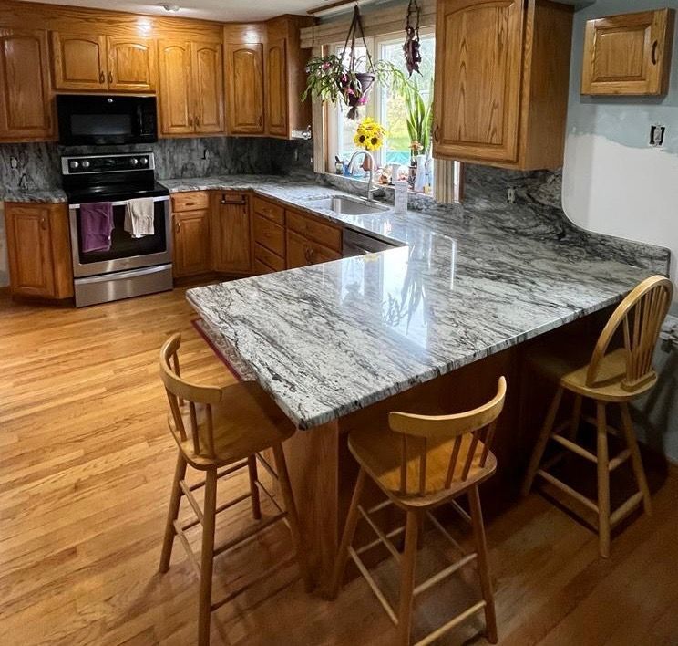 Modern kitchen with wood cabinets, stainless appliances, and a large gray-and-white marble island with stools