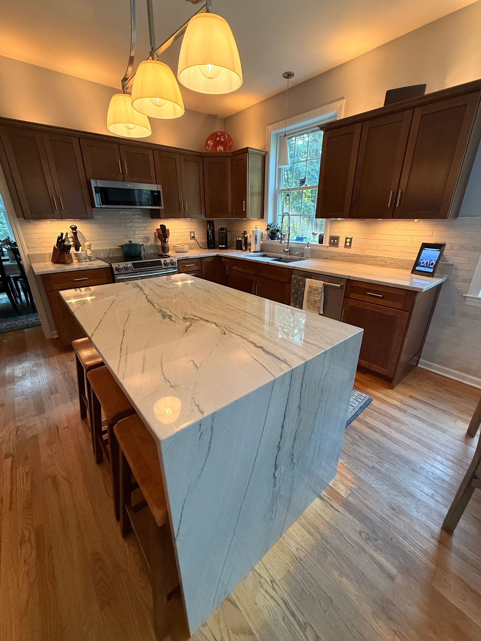 Modern kitchen with a marble island, dark wood cabinets, and warm pendant lighting.