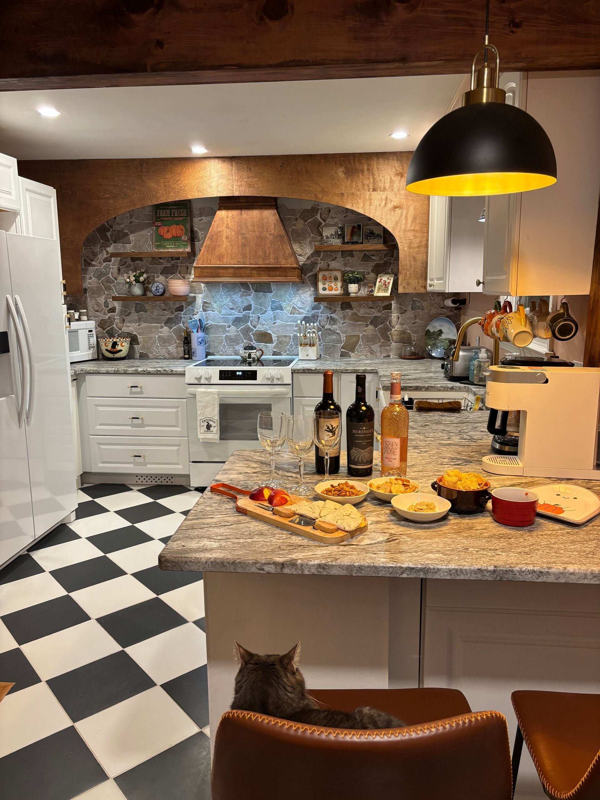 Cozy kitchen with black-and-white checkered floor, stone backsplash, island with food, and hanging black pendant lights