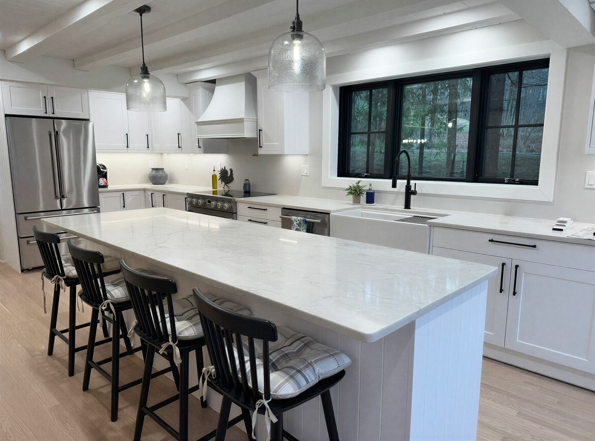 Bright modern kitchen with large white island, black stools, stainless appliances, and a wide window