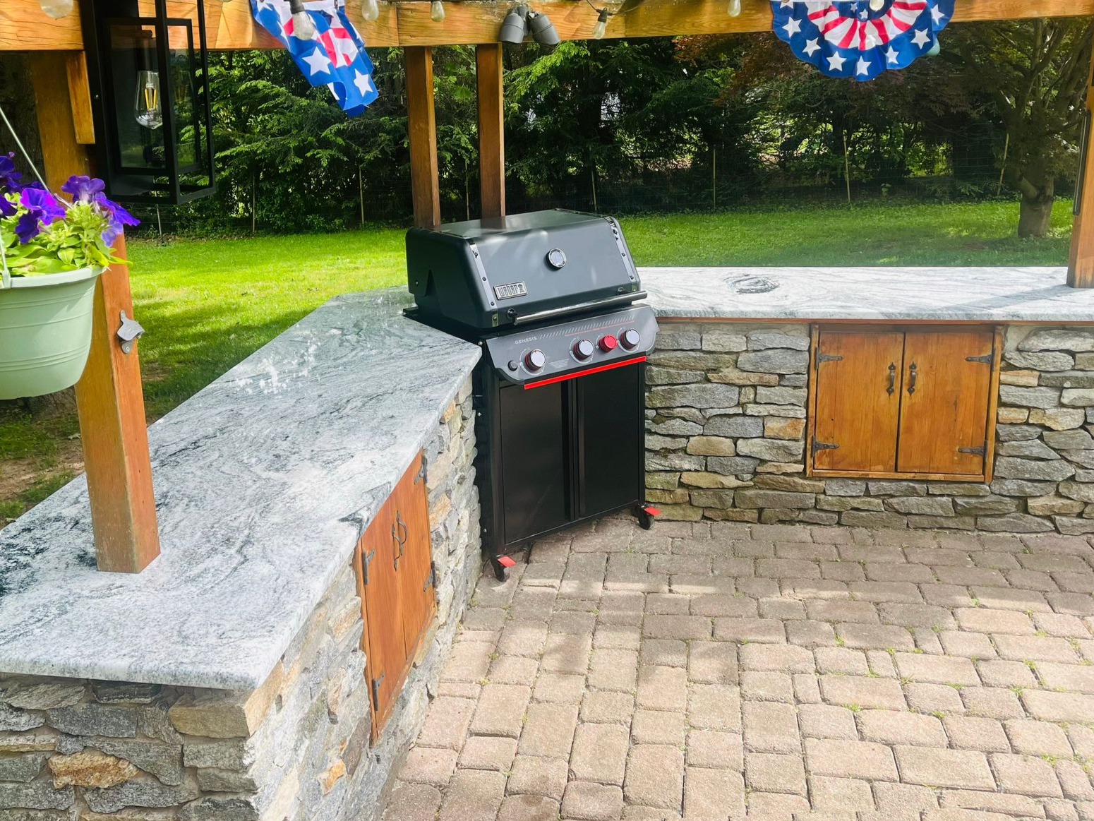 Outdoor stone patio with black gas grill beside a stone wall and lawn decorations