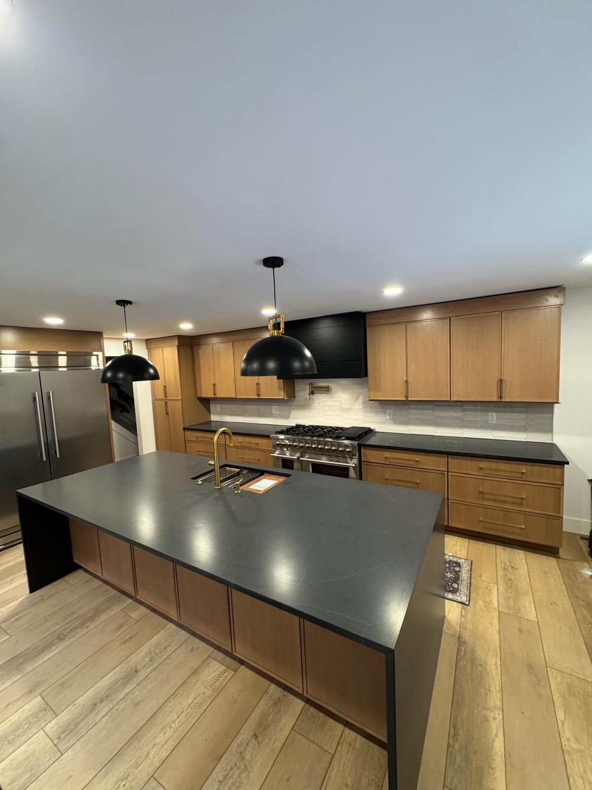 Modern kitchen with large island, dark countertops, wood cabinets, and stainless steel appliances