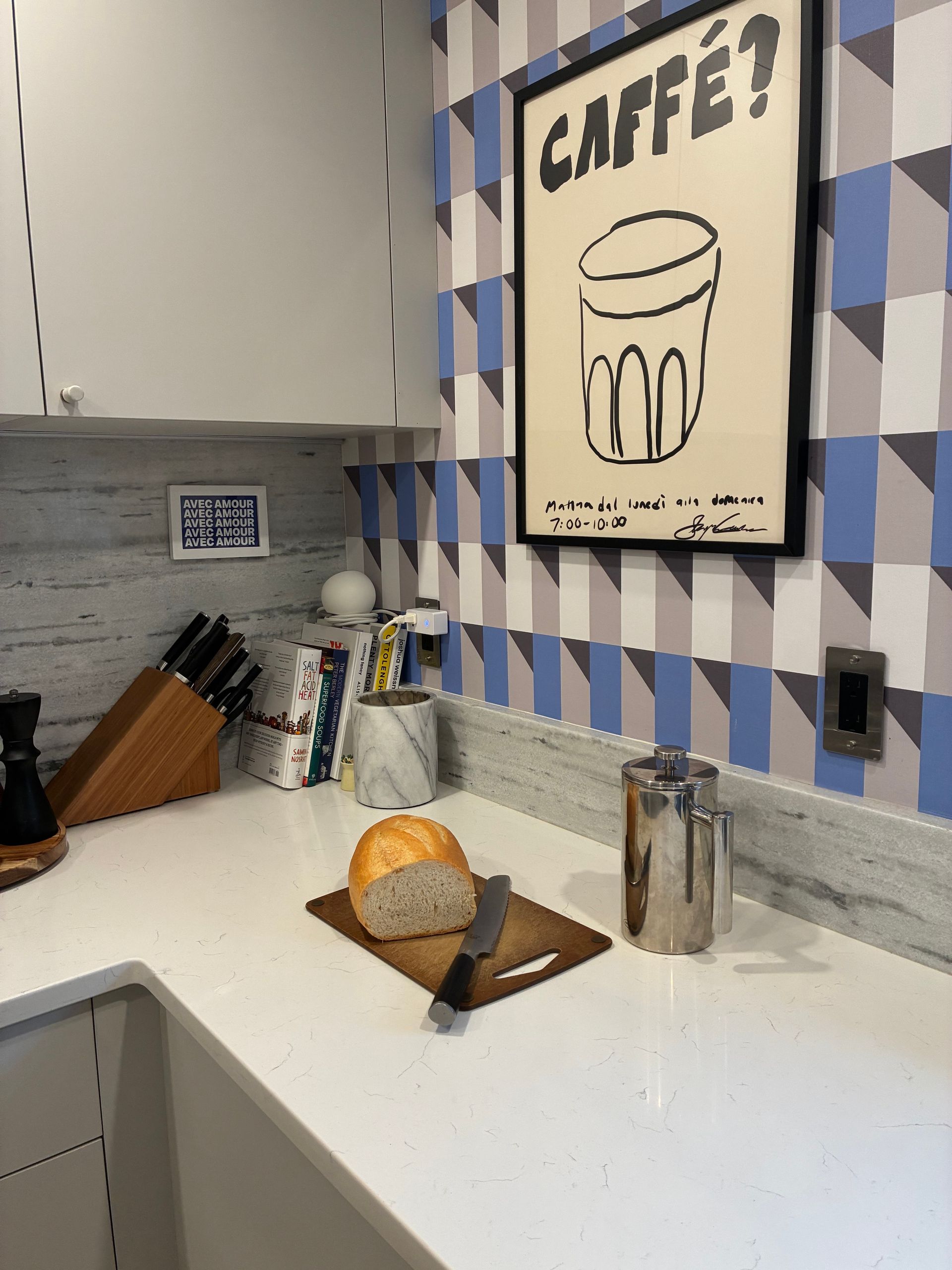 Kitchen counter with bread on a cutting board, knife block, salt shakers, and a “CAFÉ?” sign on blue-and-white tiles