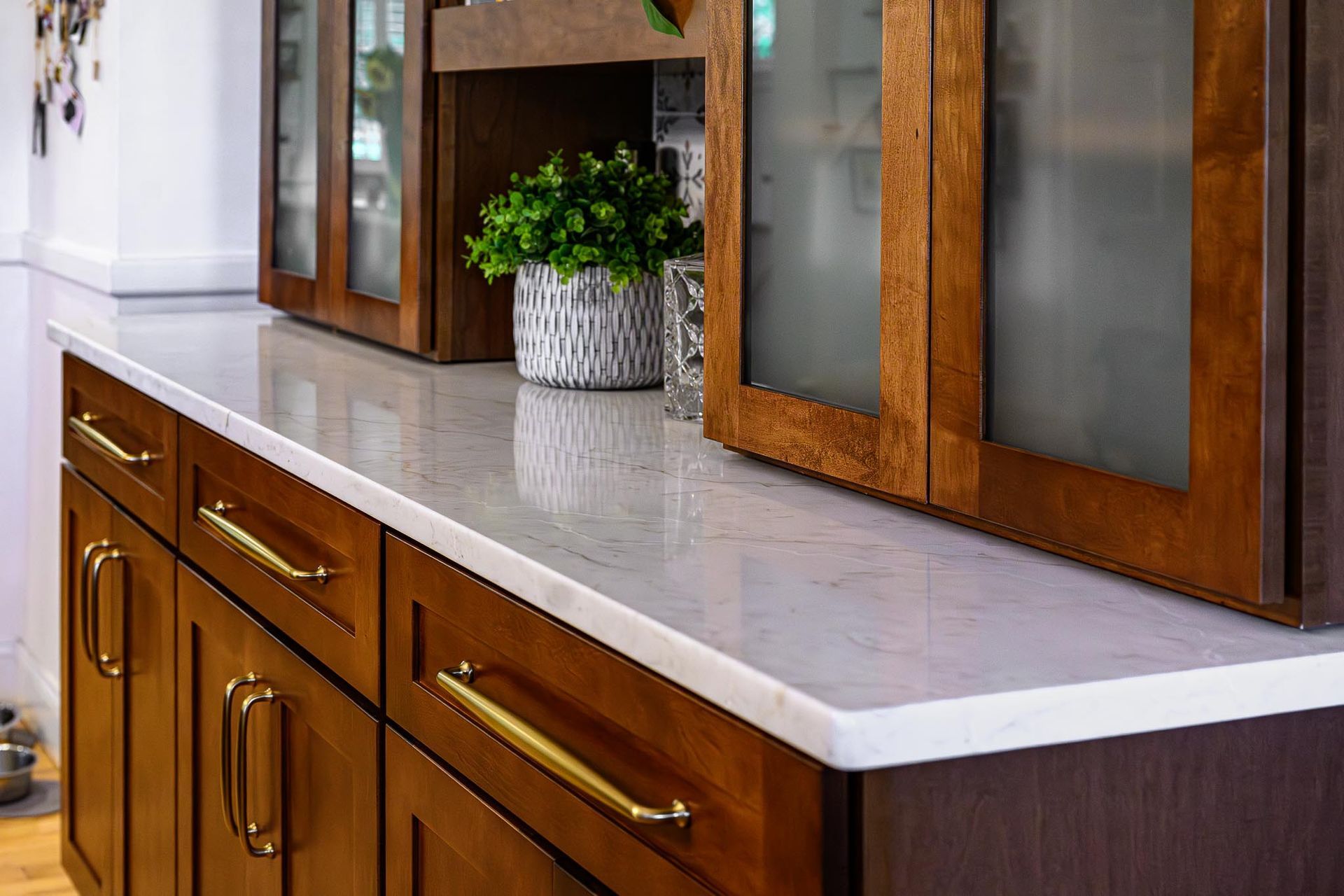 Kitchen countertop with white stone surface, wooden cabinets, and a potted plant near frosted glass cabinets