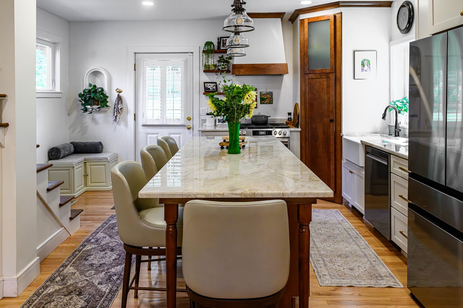 Bright modern kitchen with a large island, beige chairs, wood cabinets, and a vase of flowers on the table