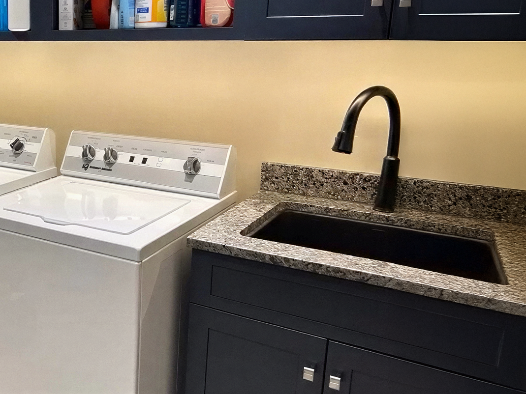 Laundry room with a white washer and a black sink cabinet under a black faucet.