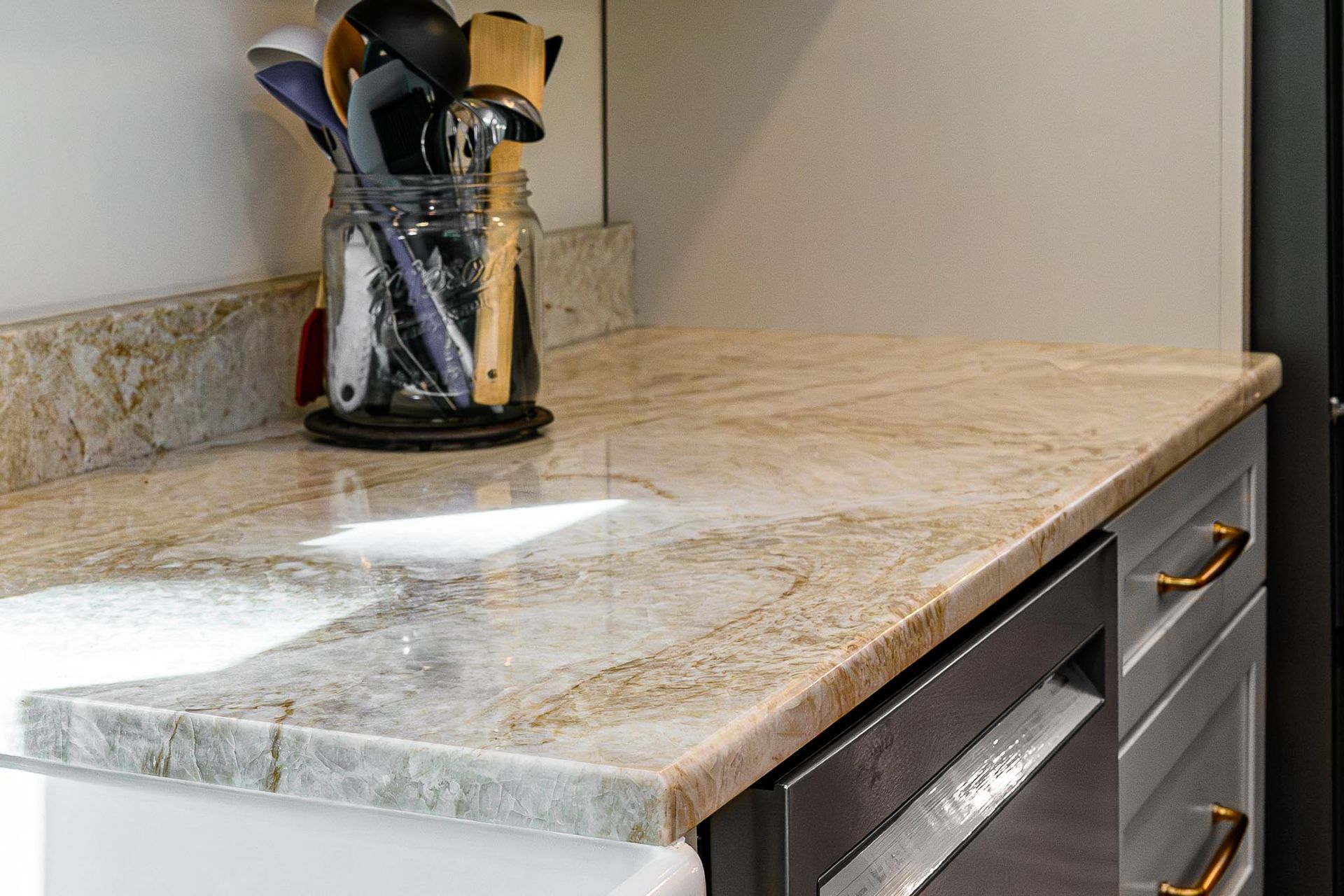 Kitchen countertop with marble surface, utensil holder, and drawers beside a sink area
