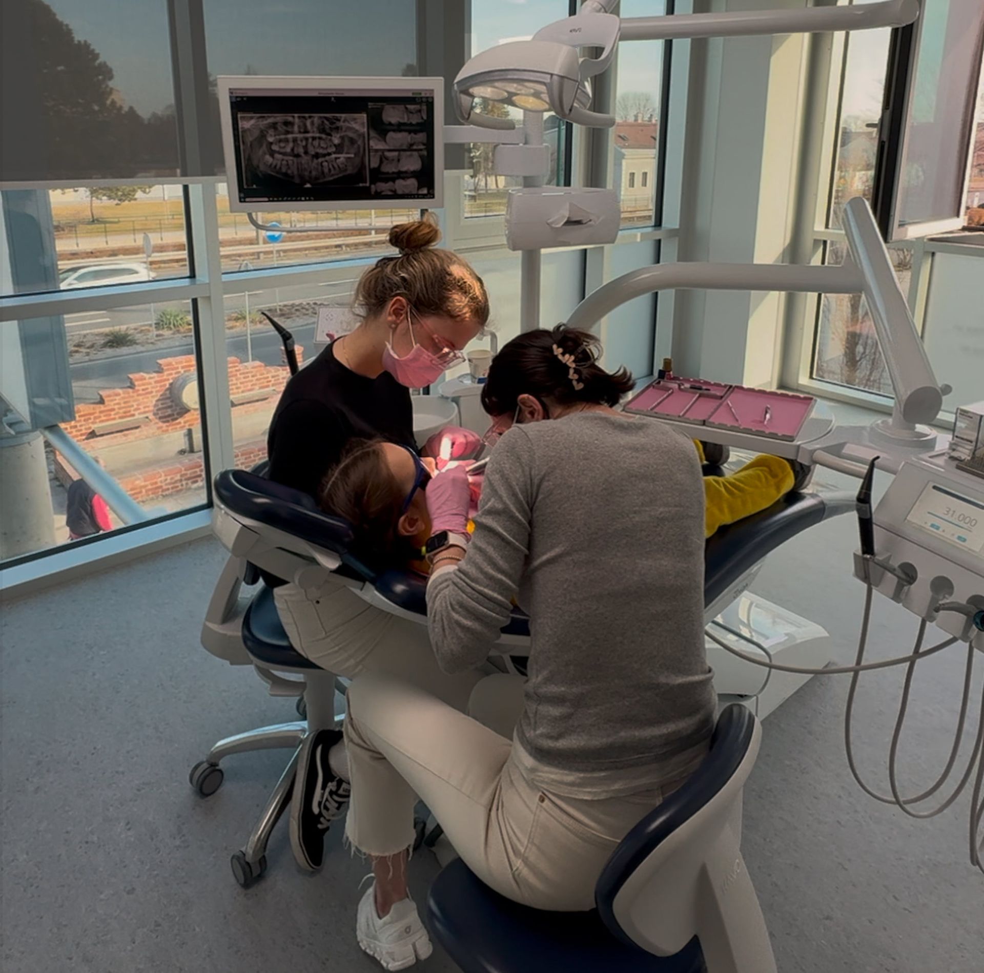 Zahnärzte behandeln ein Kind in einer Zahnarztpraxis. Ein Zahnarzt trägt eine Maske, ein anderer sitzt.