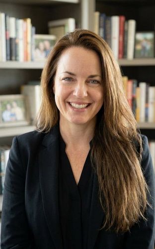Kerry Kelly in a black blazer seated in front of a bookshelf
