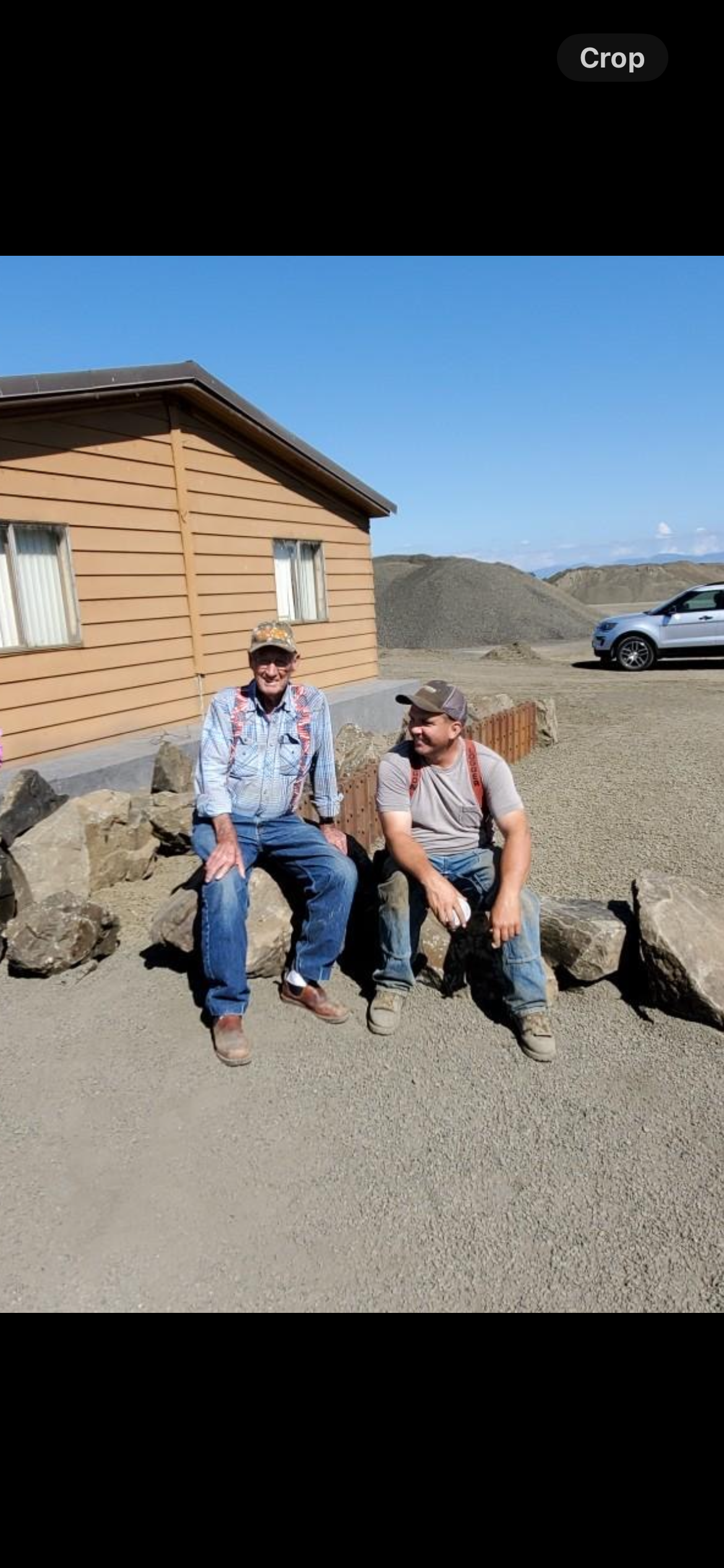 Two men are sitting on rocks in front of a house.
