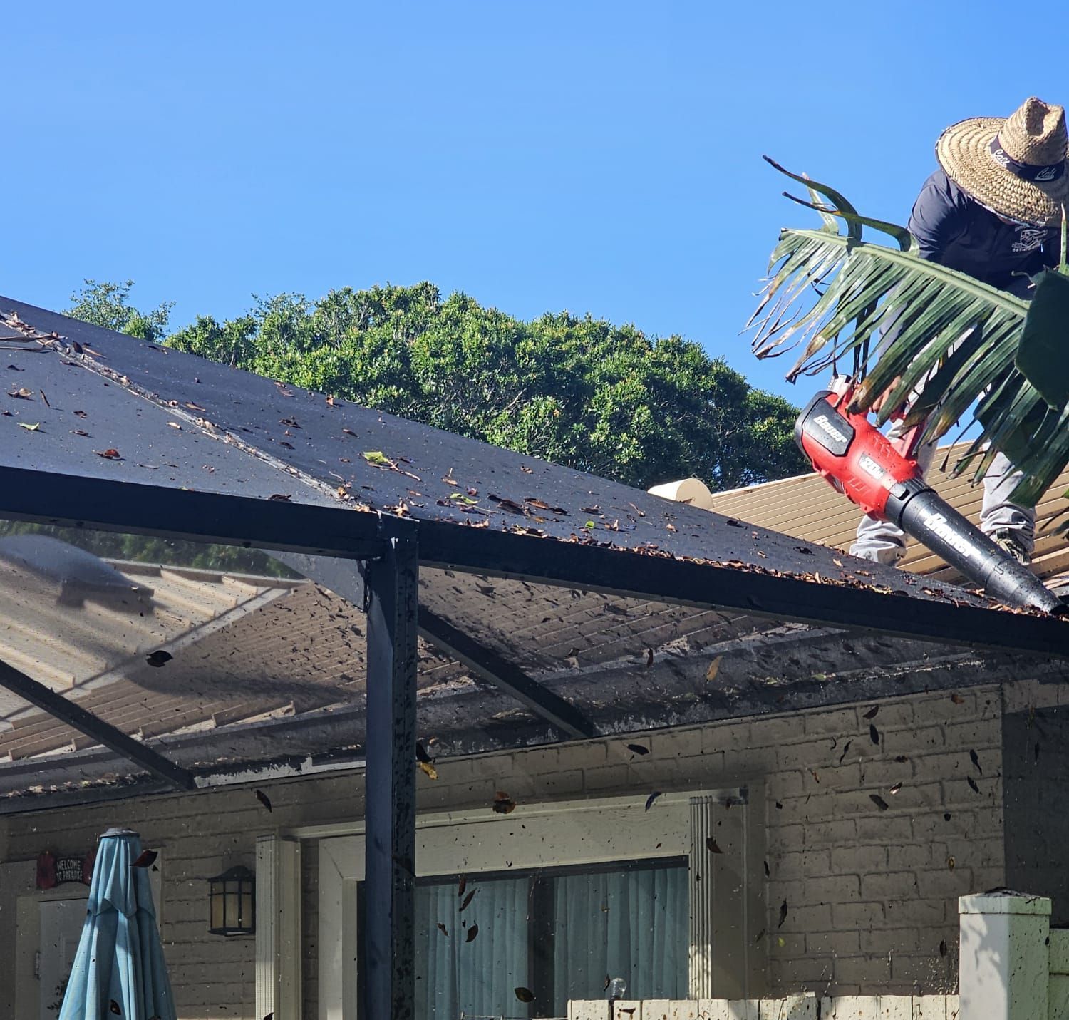 A man is cleaning the roof of a house with a blower.