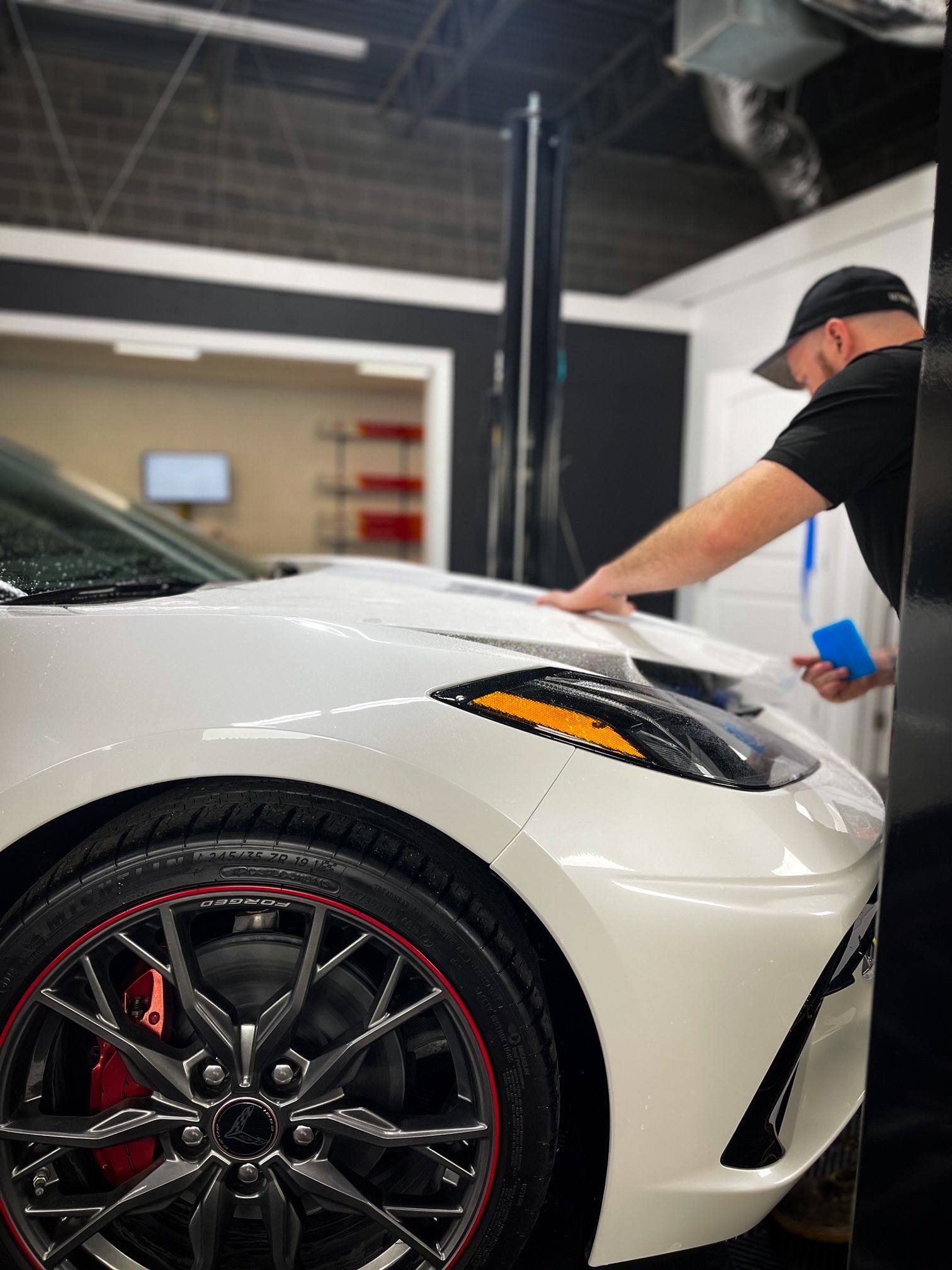 A man is applying paint protection film to the hood of a white sports car.