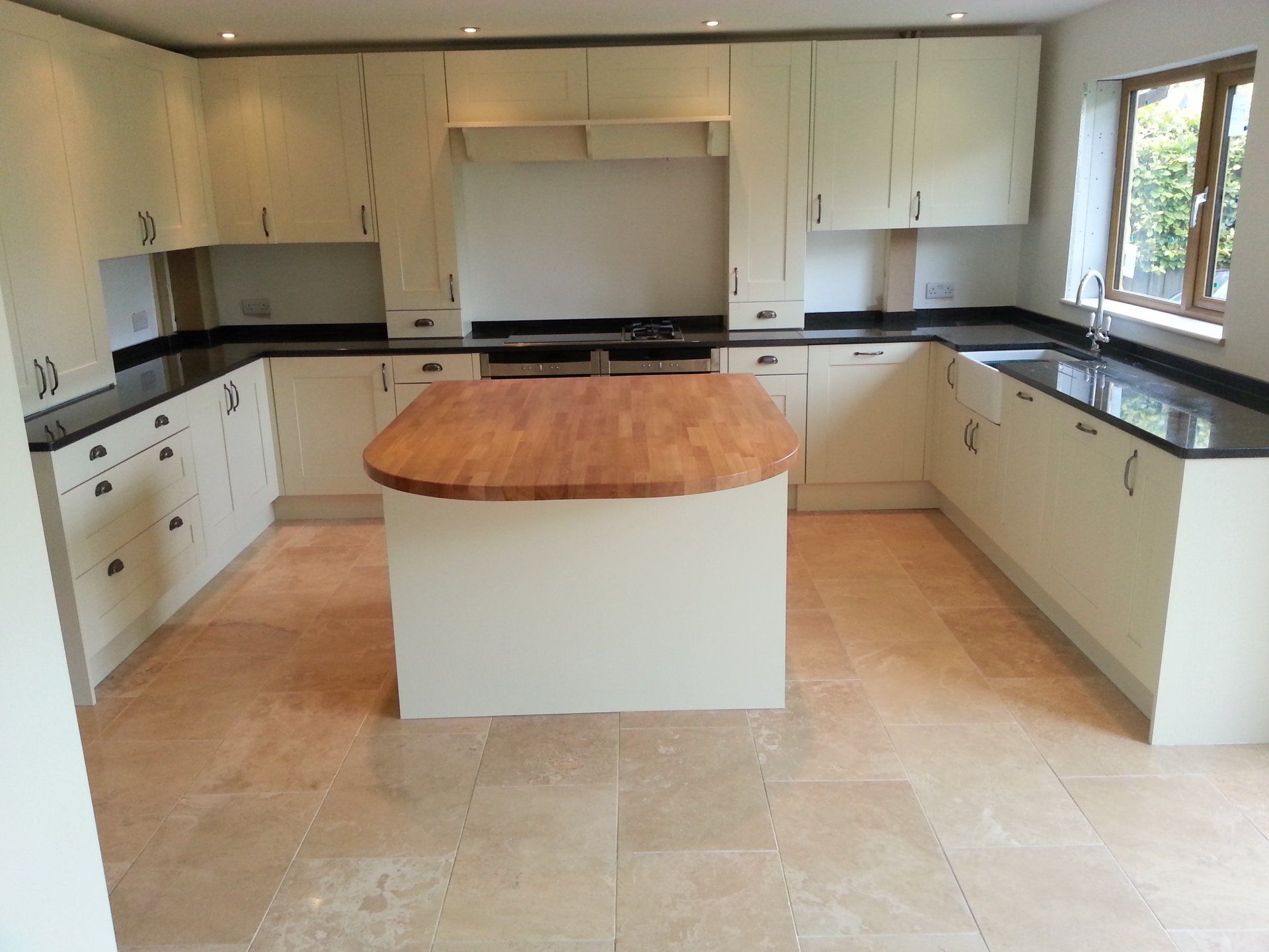 U-shaped kitchen with cream cabinets, black countertops, and a wooden island, on tiled floor.