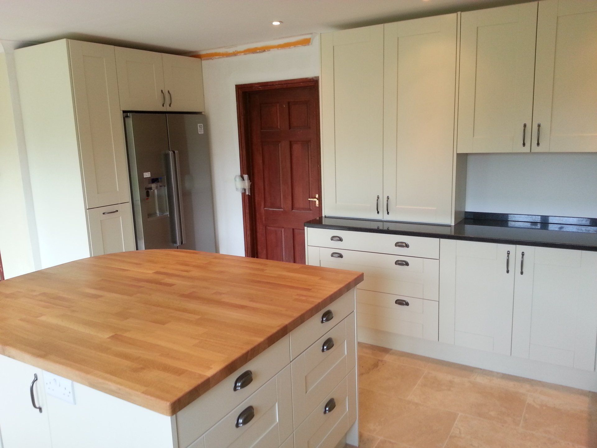 Cream-colored kitchen with butcher block island, stainless steel refrigerator, and dark countertop.