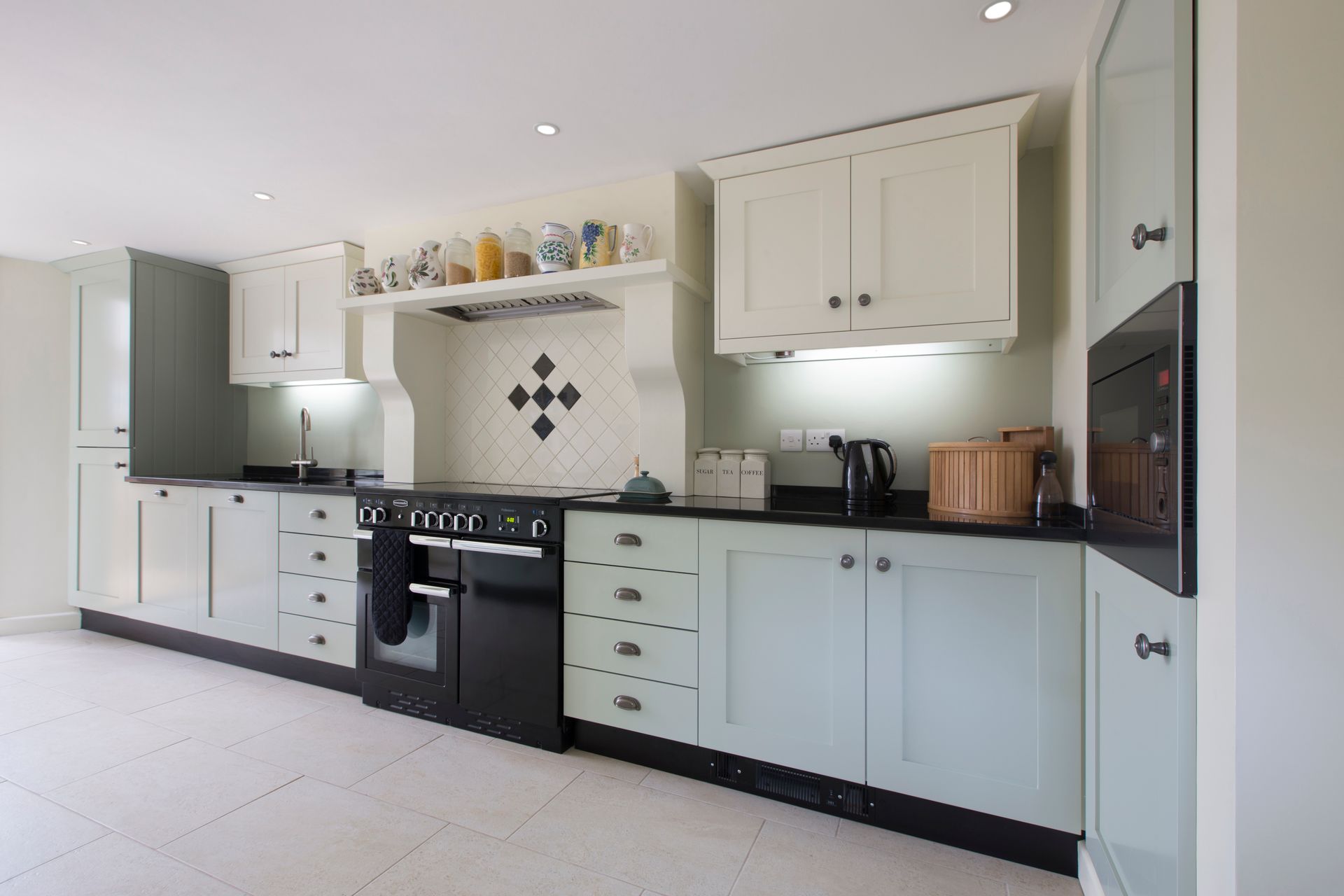 Kitchen with light blue and cream cabinets, black countertops, and a black oven.
