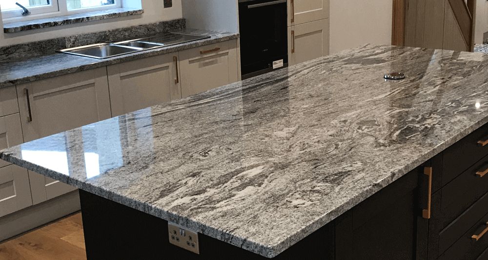 Kitchen with a black island topped with a gray and white granite countertop, beige cabinets, and a stainless steel sink.