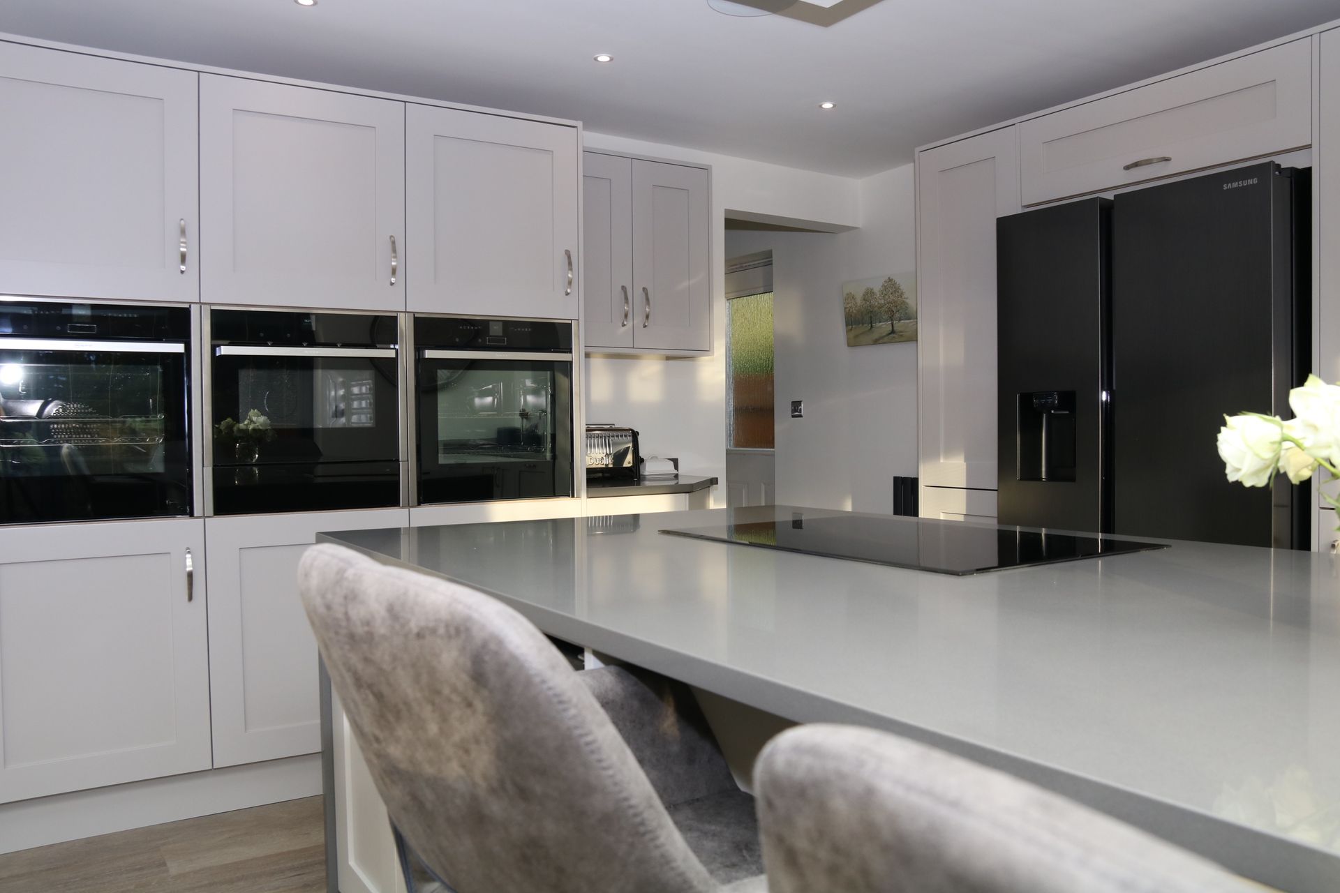 Modern kitchen with gray cabinets, island, ovens, and black refrigerator.