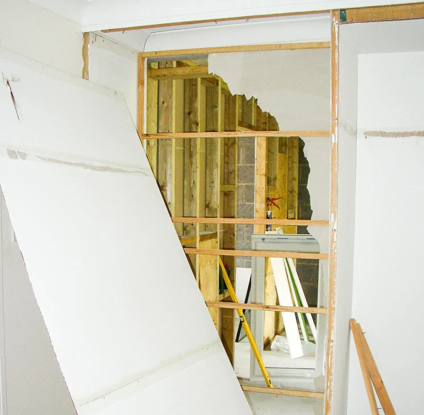 Interior wall under construction; exposed wooden frame, drywall leaning.