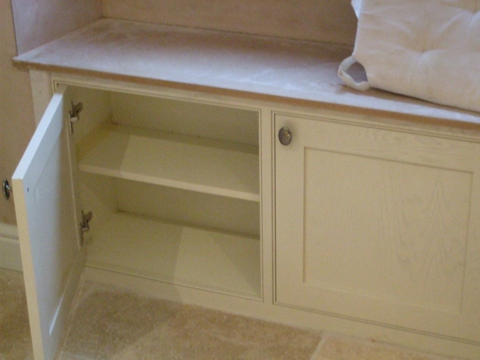 Cream-colored cabinet with open door, revealing a shelf. Cabinet sits under a countertop.