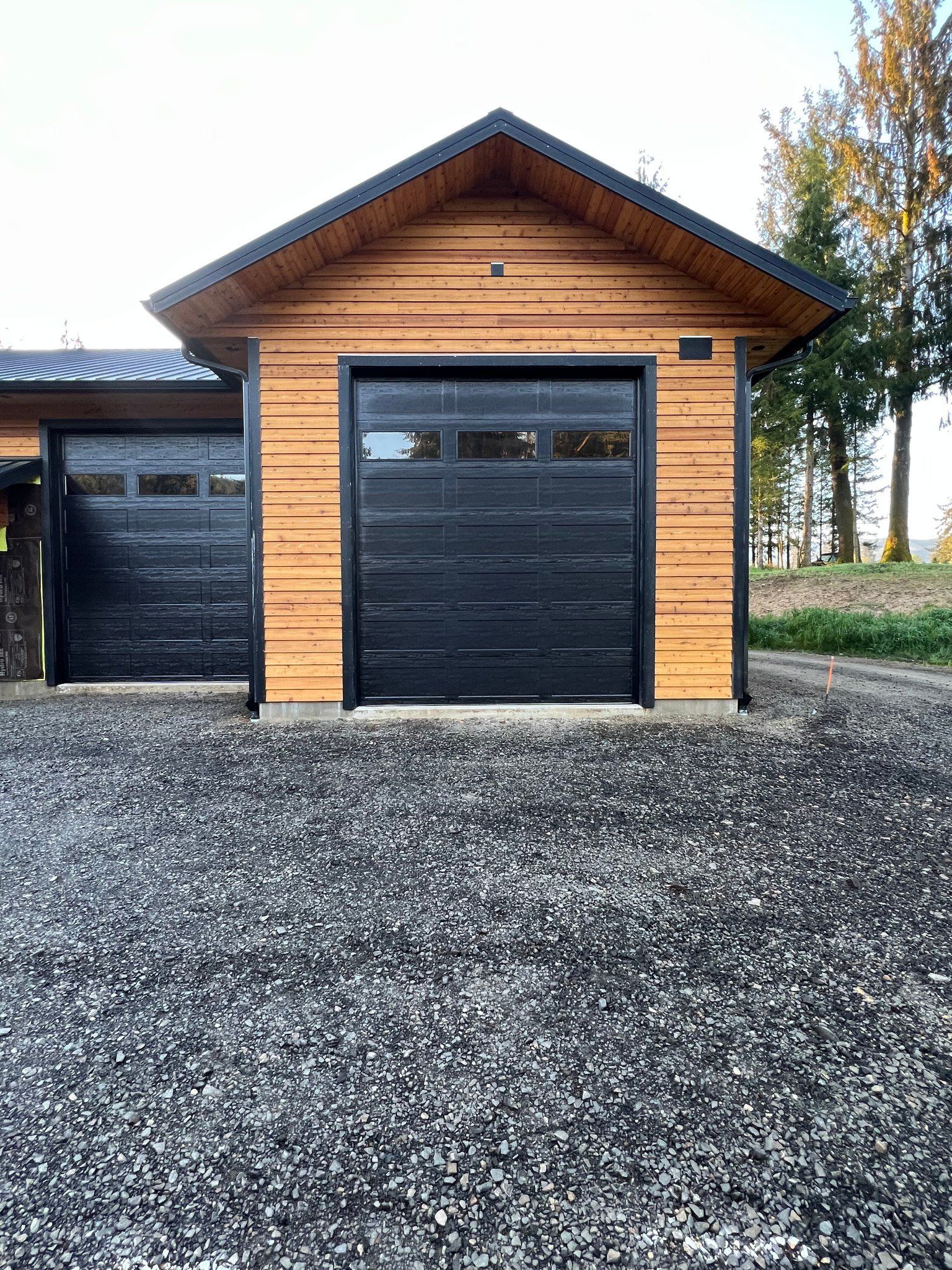 Black garage doors set in a wooden building with gravel driveway.