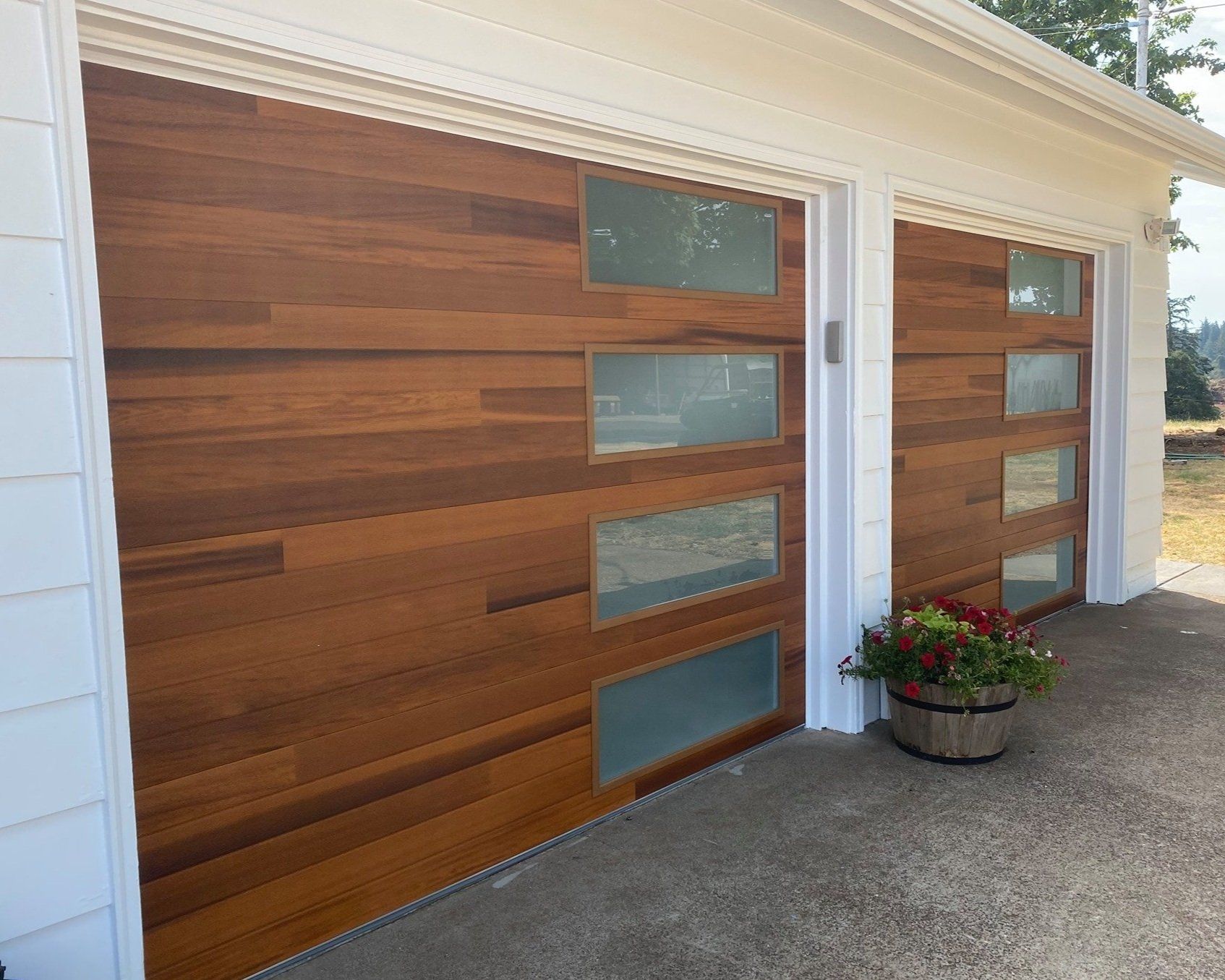 Two wooden garage doors with rectangular glass windows, flower pot in front.