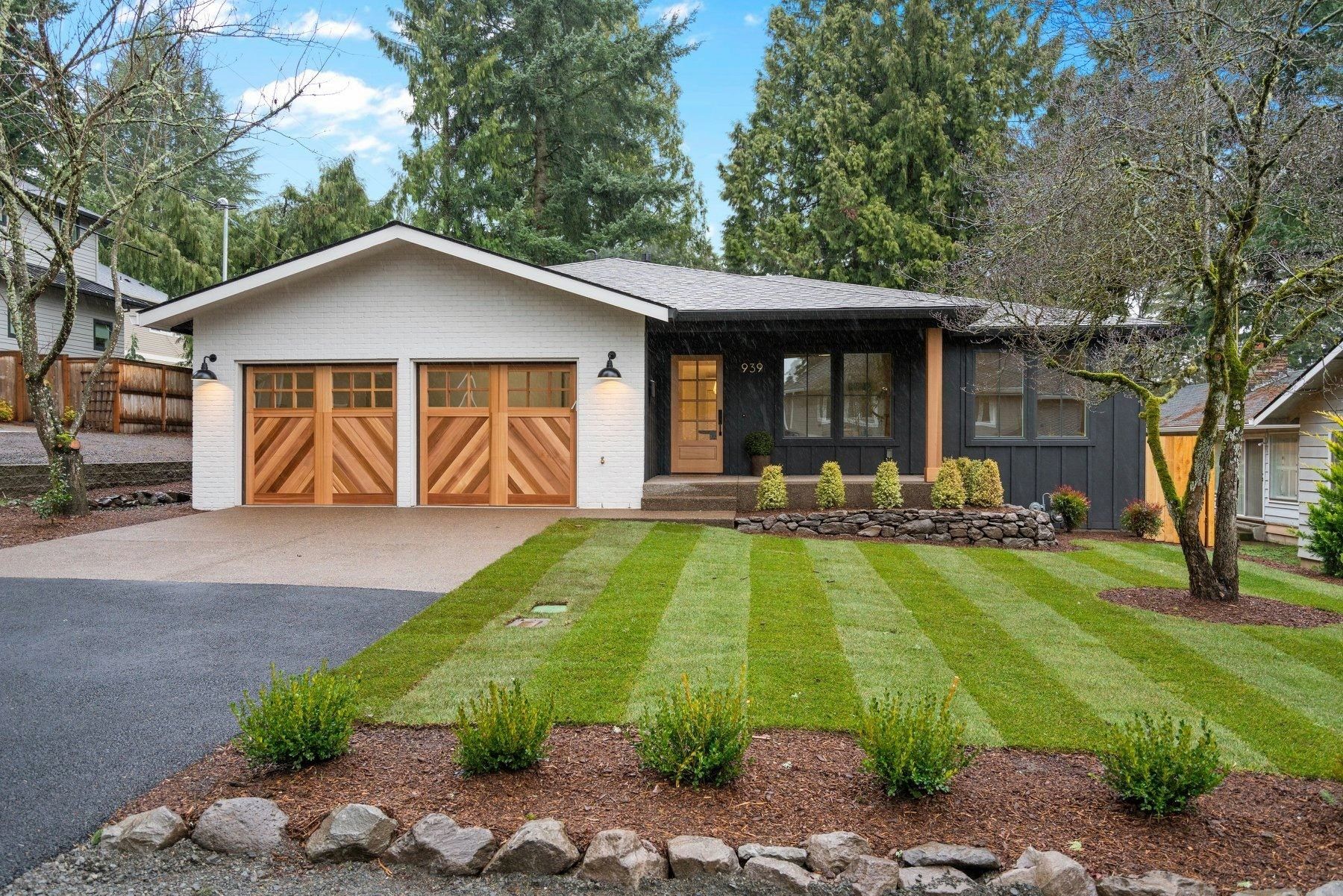 Modern single-story home with a white exterior, wooden garage doors, and a striped green lawn.
