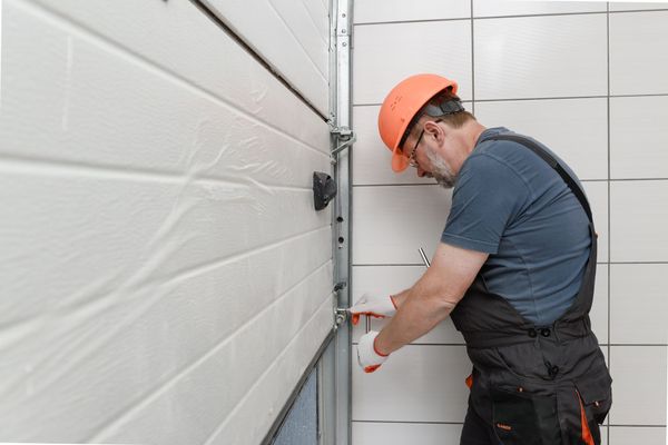 Person in overalls and hard hat repairing a white garage door.