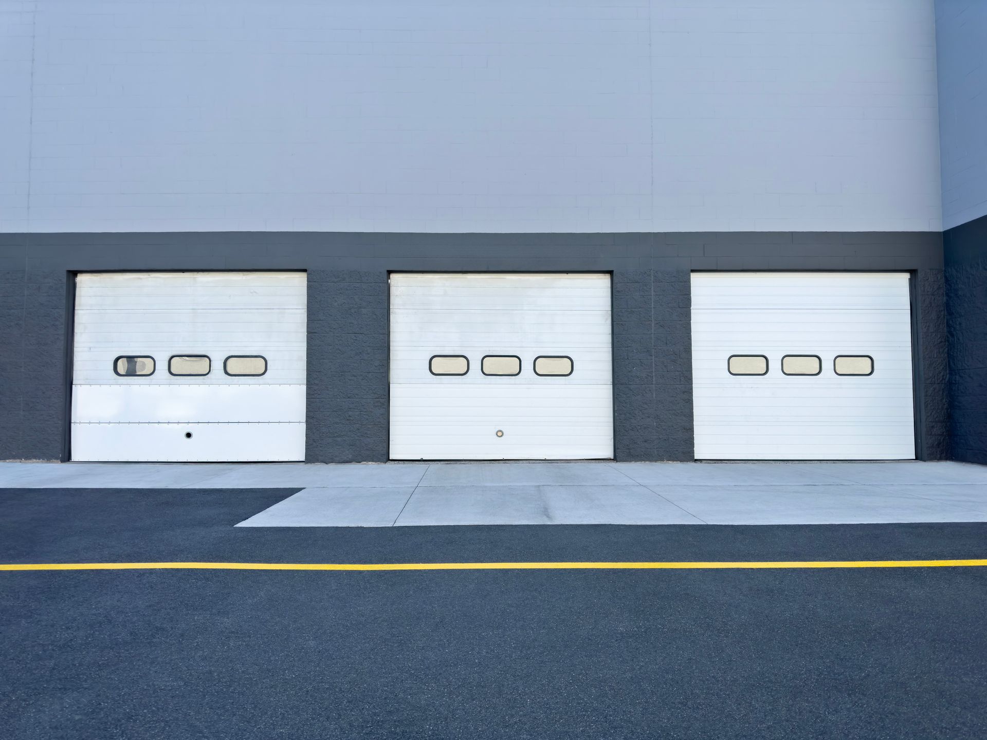 Three white garage doors with rectangular windows set in a gray and blue building.