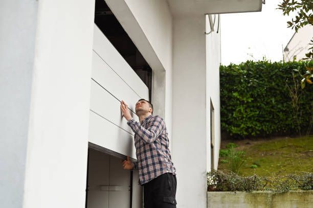 Man in plaid shirt inspecting white garage door.