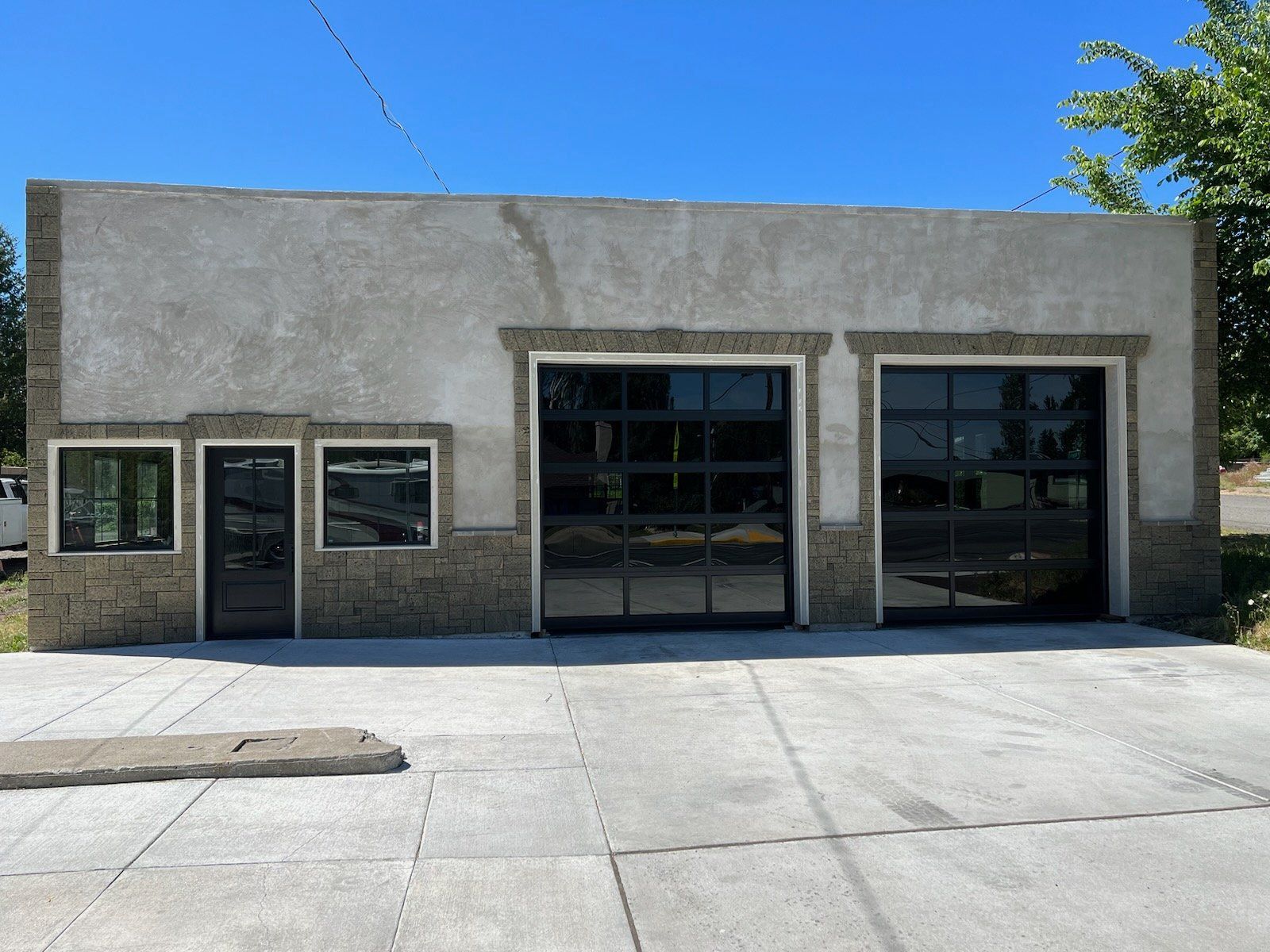 Exterior of a commercial building with glass garage doors, stone accents, and a concrete driveway under a clear blue sky.