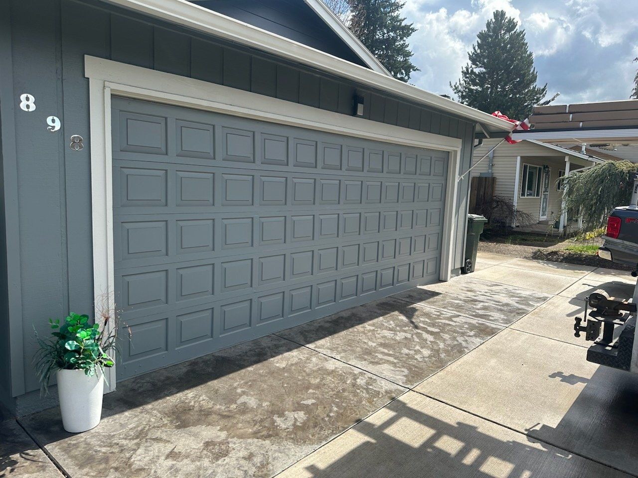 Gray garage door on a blue-gray house with white trim. Concrete driveway. Number 