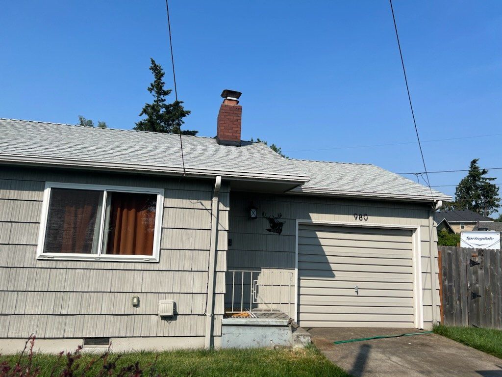 A gray-sided house with a garage, chimney, and window on a sunny day.
