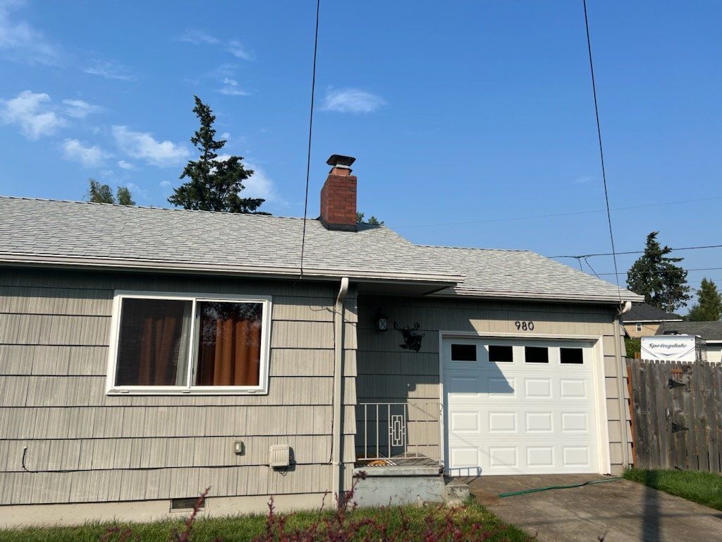 Gray-sided house with white garage door, window, and chimney against a blue sky.