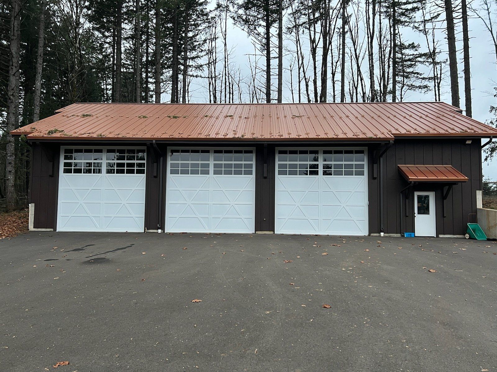 Three-bay garage with white doors, copper roof, brown siding, and small entry door.