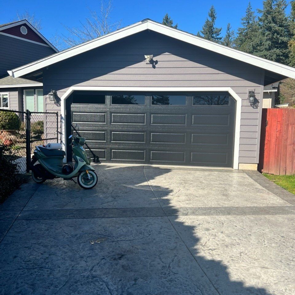 A gray garage with a black garage door and a green scooter on the driveway.