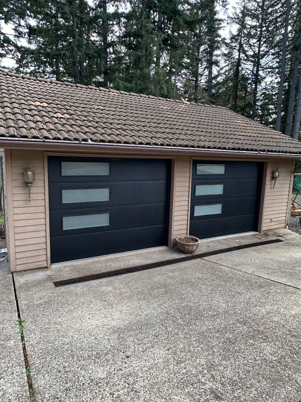 Two black garage doors with frosted glass panels on a concrete driveway, under a tile roof.