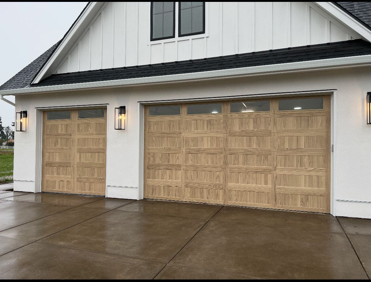 Two tan garage doors on a white house, opening. Black roof and sconces present.