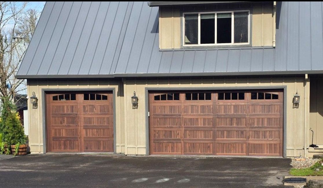 Two-car garage with brown wooden doors and a gray metal roof, with an upper story and a driveway.