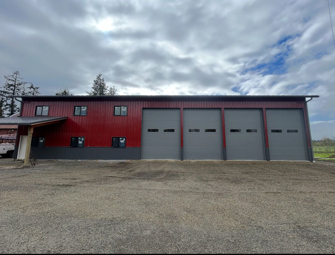 Red metal building with gray garage doors under a cloudy sky.