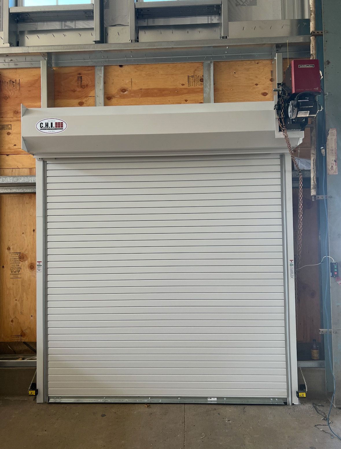 White rolling shutter door, partially open. Motor and mechanism visible at top right.