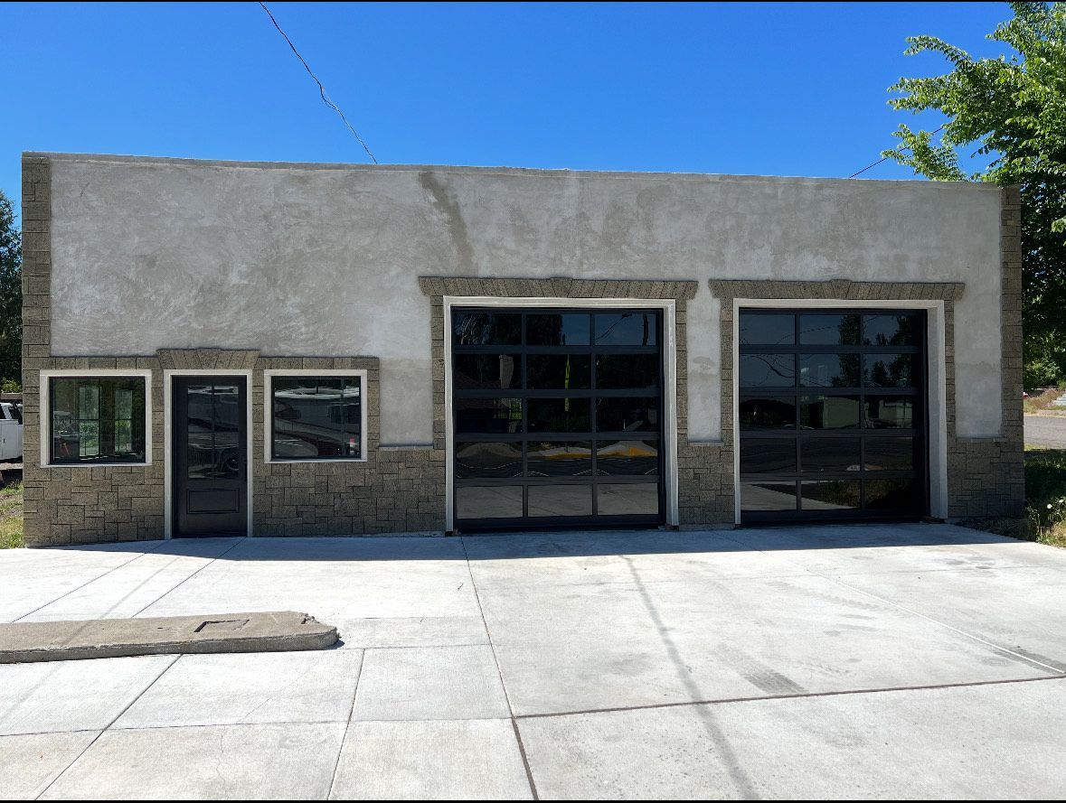 Exterior view of a commercial building with two garage doors and a small office entrance, all with dark glass.