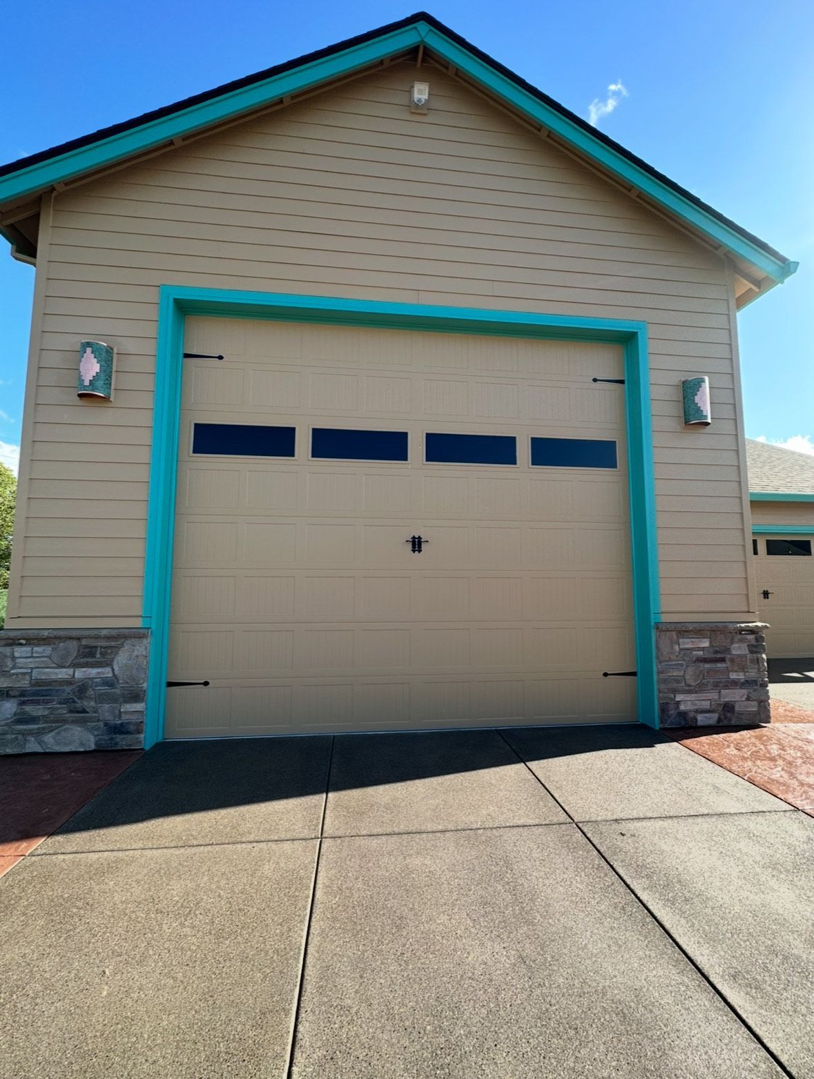 Tan garage with teal trim and black windows, brick base, and concrete driveway.