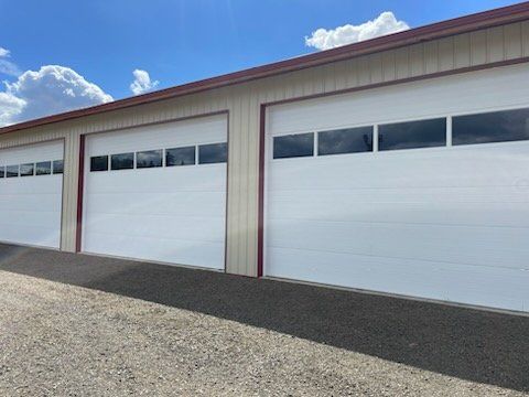Three white storage unit doors with window panels under a blue sky.