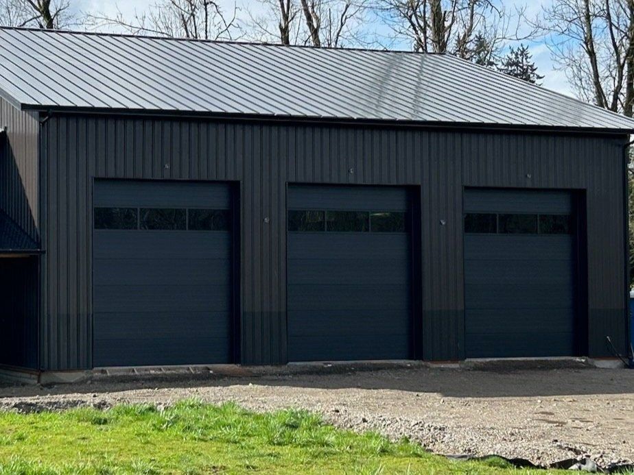 Dark gray three-bay garage with matching garage doors and a corrugated metal roof.