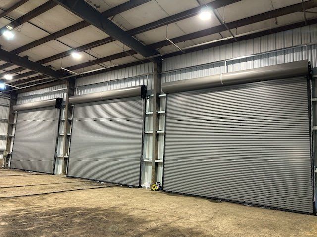 Three closed, gray roll-up doors in a large metal warehouse with overhead lighting.