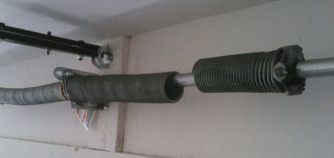 Garage door torsion spring, coiled, mounted horizontally on a wall.