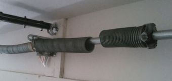 Garage door torsion spring, coiled, mounted horizontally on a wall.