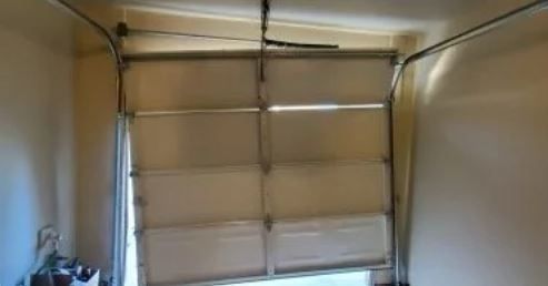 Garage door, partially open and crooked, in a beige-walled garage.